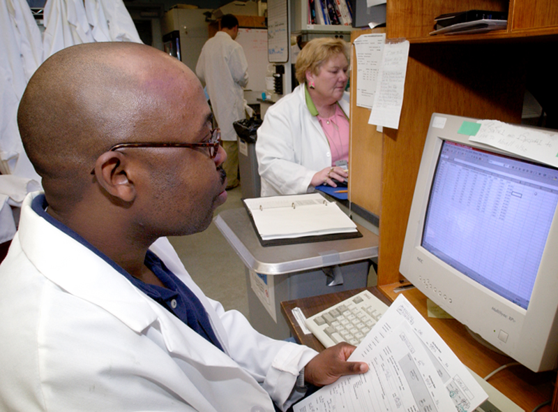 This image depicts CDC researchers as they review incoming SARS data using a SPB diagnostic laboratory computer workstation in the foreground, while in the background, the data entry is being carried out.
