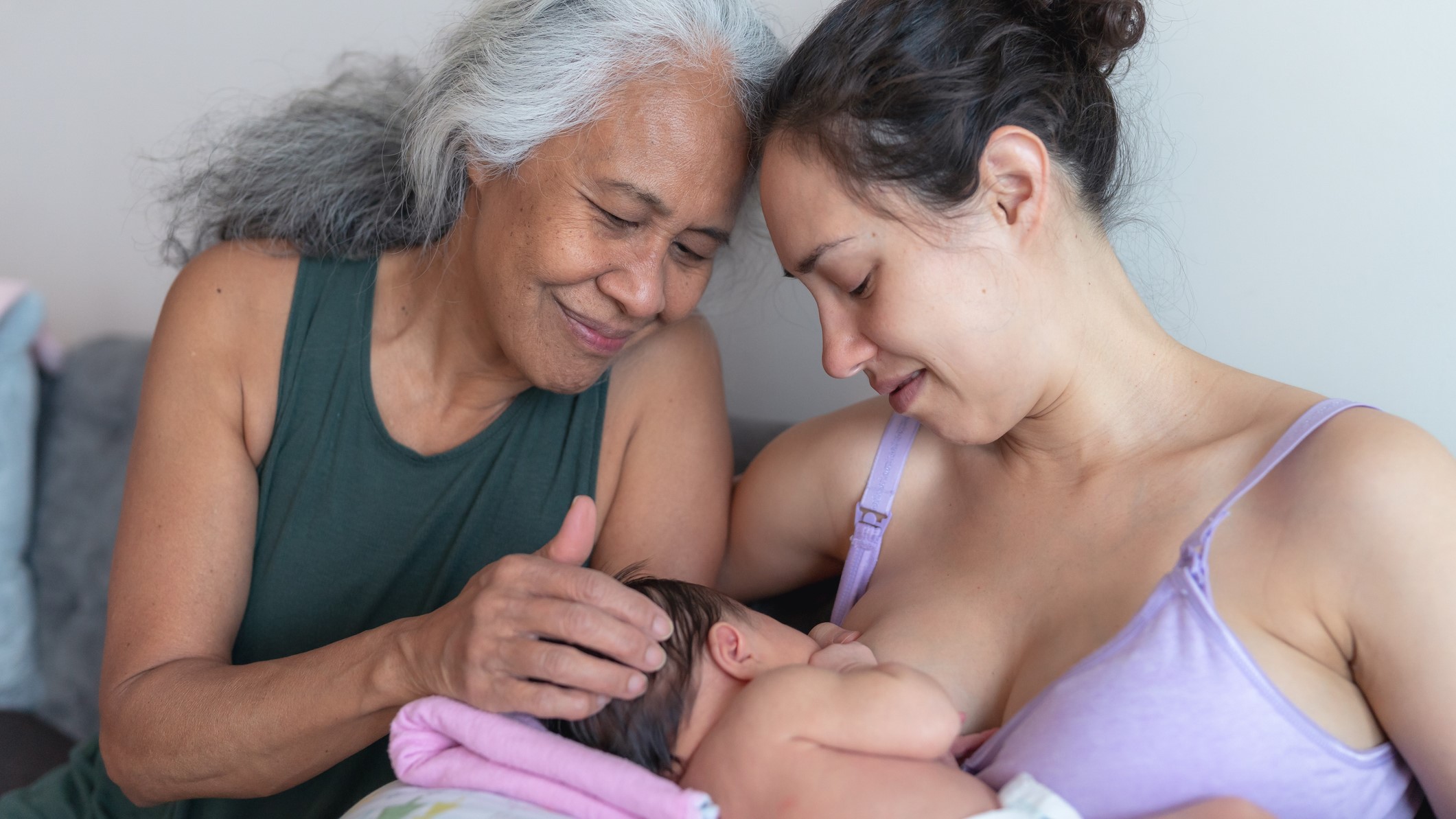 A young mother breastfeeding baby with encouragement from an older woman.