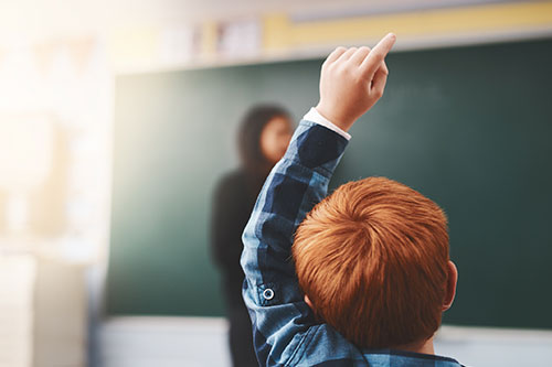 Red-headed child raising his hand in class