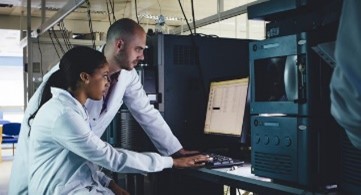 Two people wearing lab coats working on computer