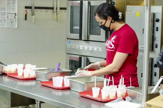 A school district worker plating healthy food in a cafeteria.