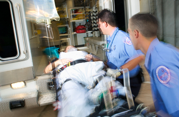 EMTs lifting a patient on a gurney into the back of an ambulance.