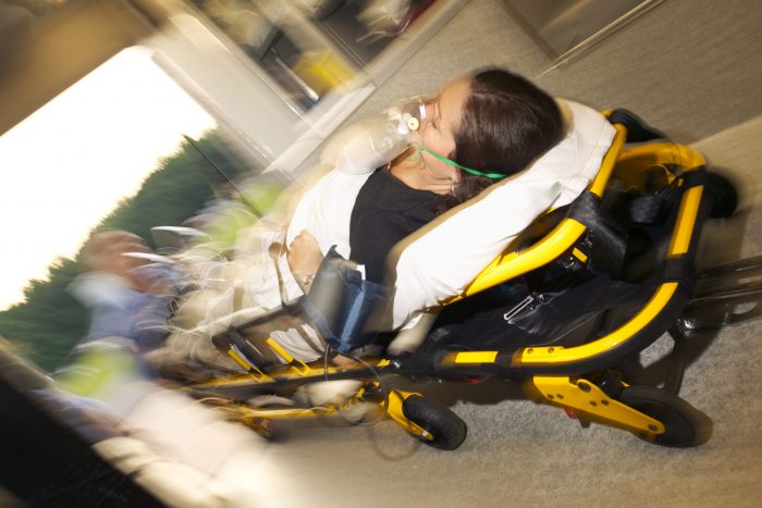A patient on a stretcher is loaded by medics into an ambulance.