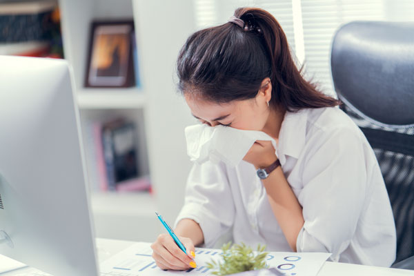 woman at a work desk sneezing into a tissue