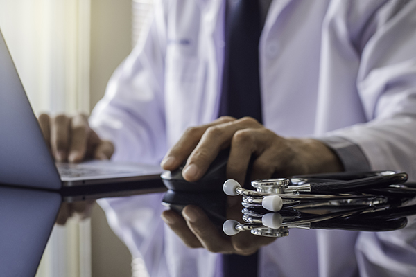 A male doctor working on his computer with stethoscope on the desk.