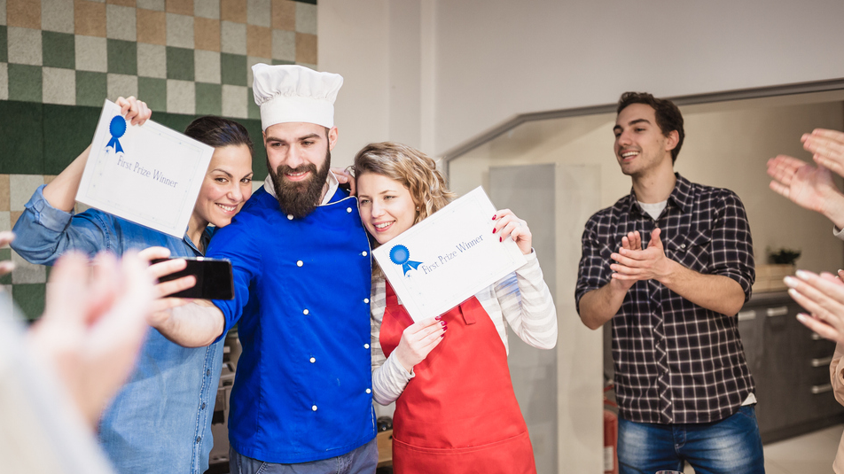 Chef and kitchen staff taking a selfie after receiving recognition with audience applauding.