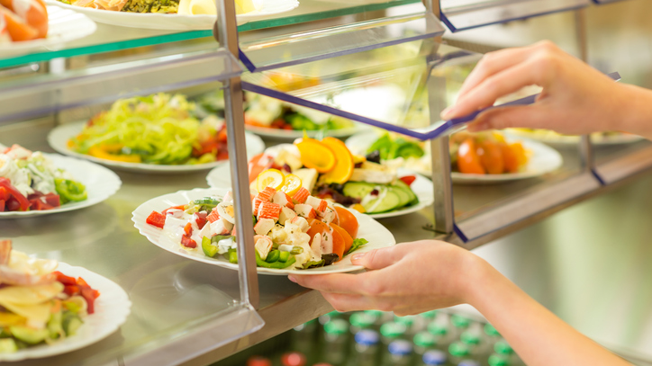 Close up of hands getting a salad in a food service setting