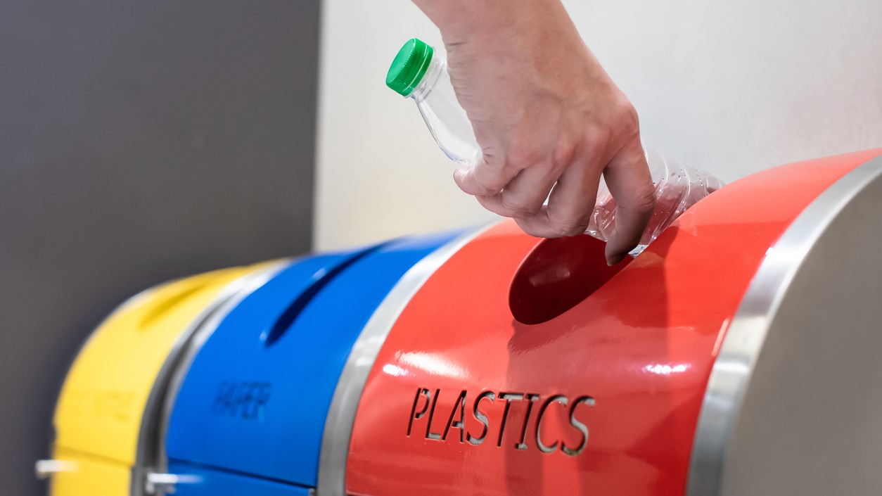 Person putting plastic bottle in recycling bin.