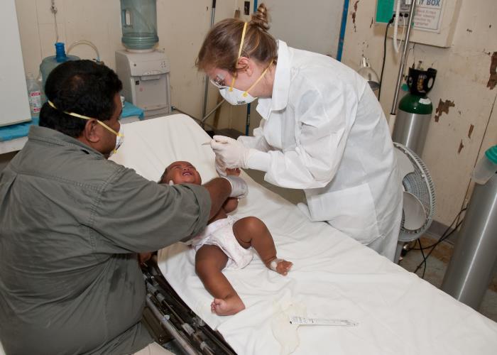 Created in June, 2014, by Centers for Disease Control and Prevention (CDC) Medical Epidemiologist, Umid Sharapov, M.D., M.Sc., this image depicts CDC Epidemic Intelligence Service (EIS) Officer, Lucy Breakwell, Ph.D., M.Sc., wearing the appropriate personal protective equipment (PPE), which included a face mask, gloves, and a lab coat, as she was in the process of obtaining a nasopharyngeal swab from a child with measles, on the island of Kosrae, part of the Federated States of Micronesia (FSM). FSM is an independent sovereign island nation in the Western Pacific Ocean. No measles cases were reported in 20 years before this outbreak. When the first cases were reported, a CDC Epi-Aid team was dispatched to investigate the outbreak. There were 371 cases reported on three islands, over a 6 month period. This was one of the entries in the 2015 CDC Connects, Public Health in Action Photo Contest.