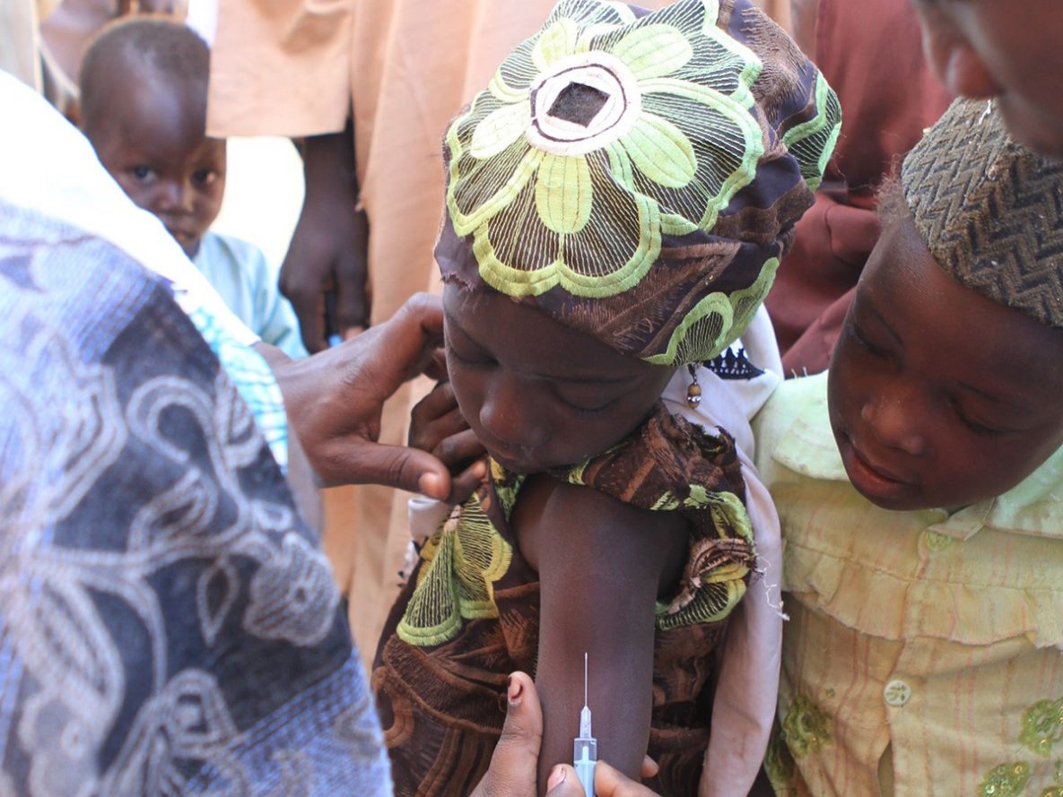 In Nigeria, a little girl prepares to receive her measles vaccination while other children watch.