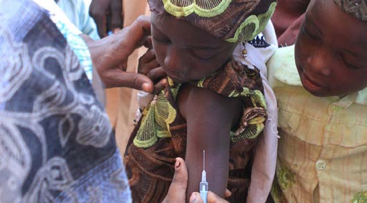 In Nigeria, a little girl prepares to receive her measles vaccination.