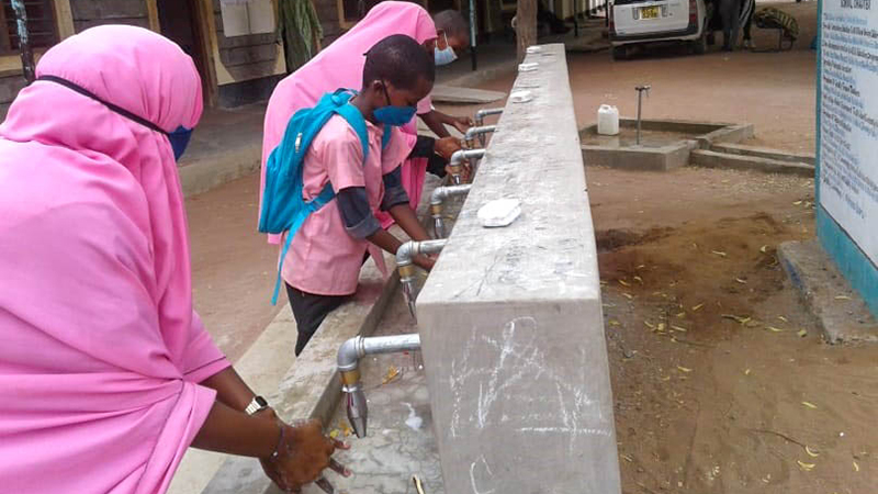 Two girls and one boy wash their hands at a washing station