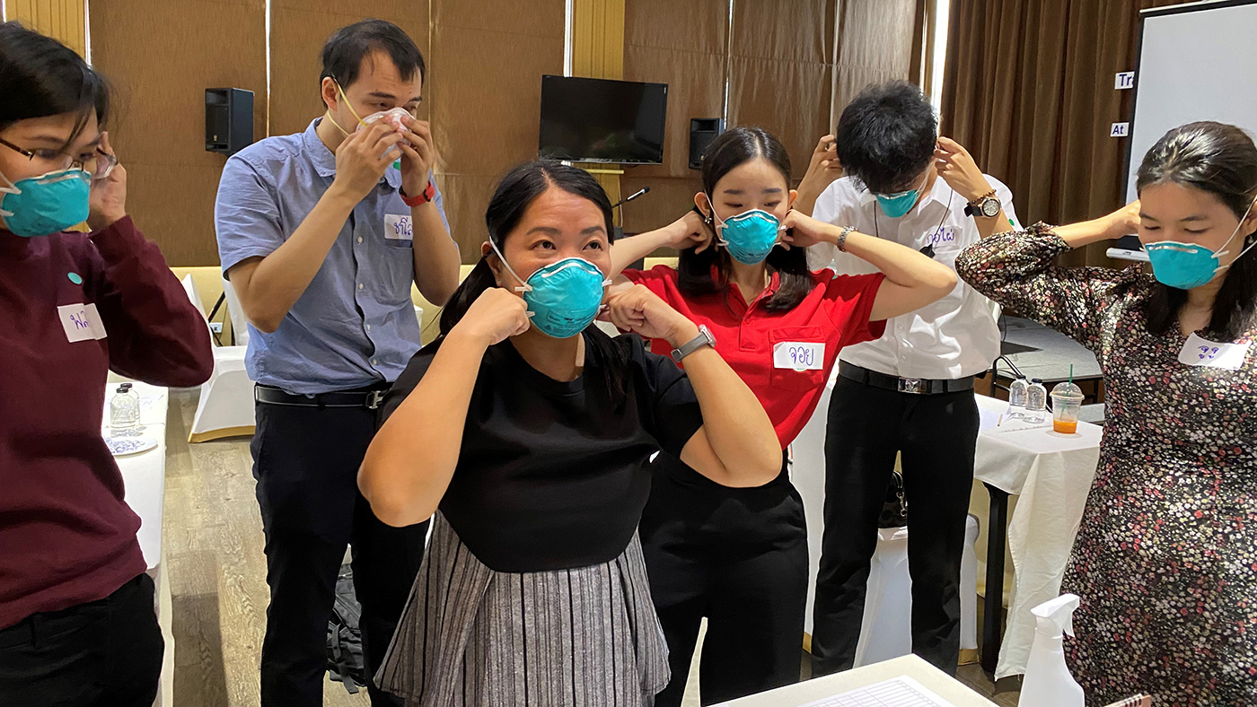 A CDC Thailand staff member demonstrates how to properly put on and take off an N-95 mask as part of public health worker training.