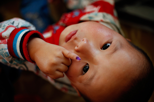 A young baby holds his finger to show that he's been vaccinated.