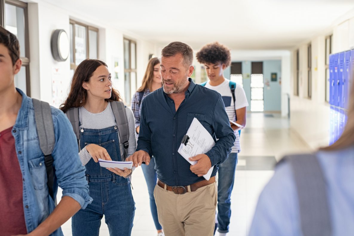 High school student talking to teacher in school hallway