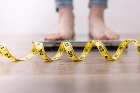 Photo of feet on a scale with a tape measure along floor.