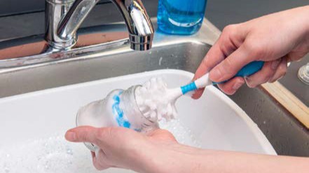 A person washing a bottle with a scrub brush.