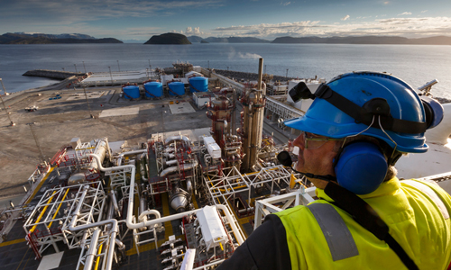 Oil industry worker wearing noise protection looking out over a large facility