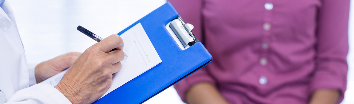 Female doctor writing on clipboard in clinic with female patient