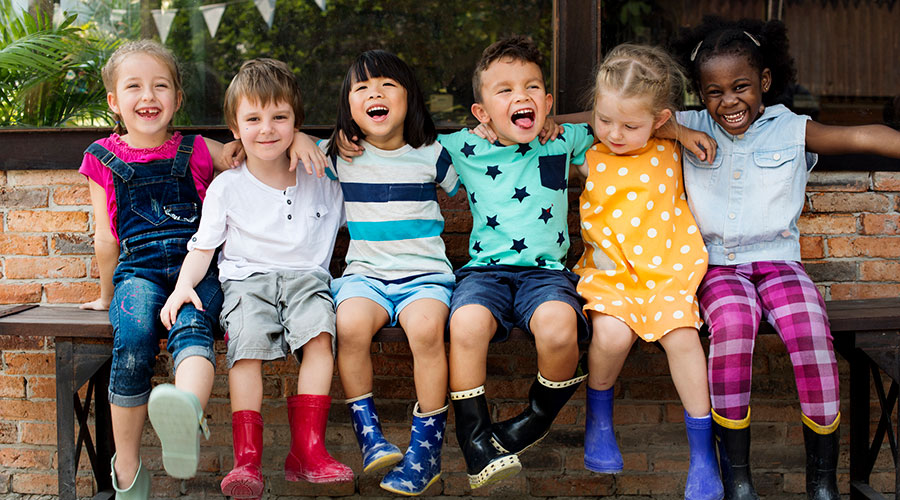 Diverse group of happy children sitting on a park bench in rain boots