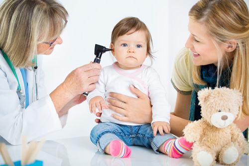 Doctor examining toddler's ear with mom smiling