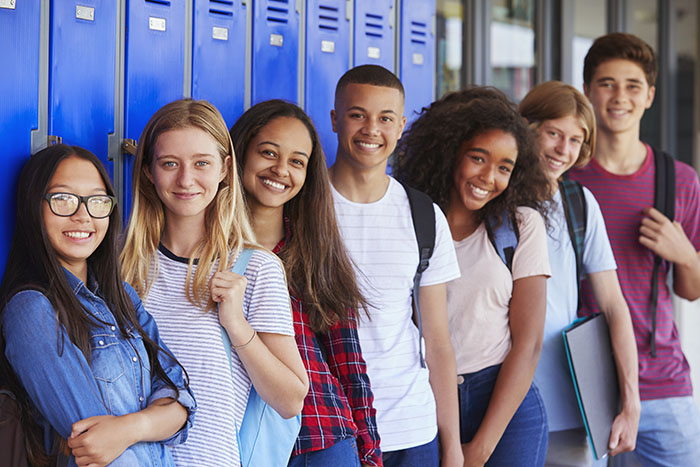 Teenage school kids smiling to camera in school hallway