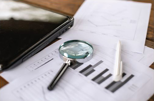 Magnifying lens with black and white spreadsheets and a closed black laptop