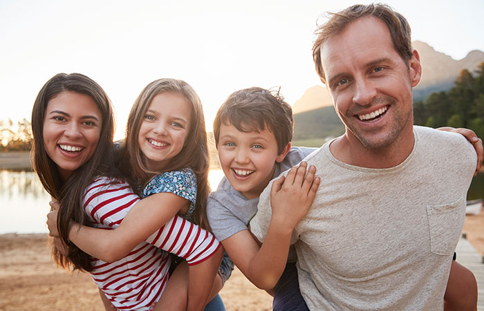 a happy family. The parents are giving their son and daughter a “piggy-back” ride in the countryside.