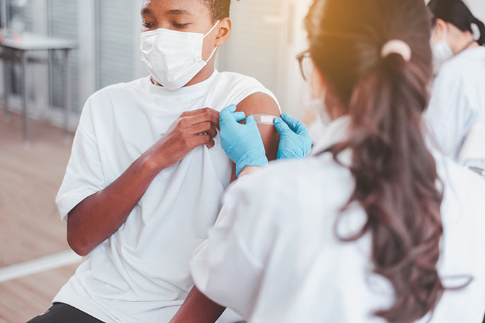 Doctor putting bandage on arm African American boy after getting a flu vaccination.