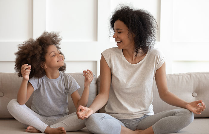 Happy african american woman teaching little daughter meditating and practicing yoga exercises.