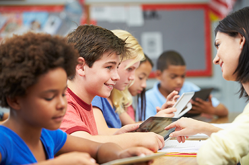 Students in class using digital tablets with a teacher