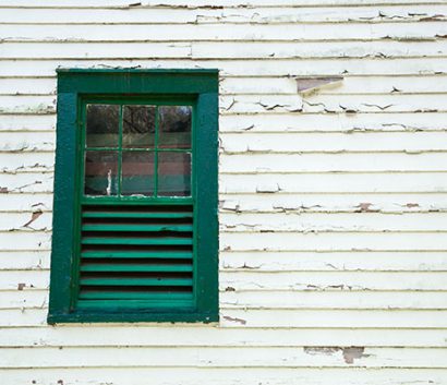 Detail of side of building shows peeling paint and an old window.