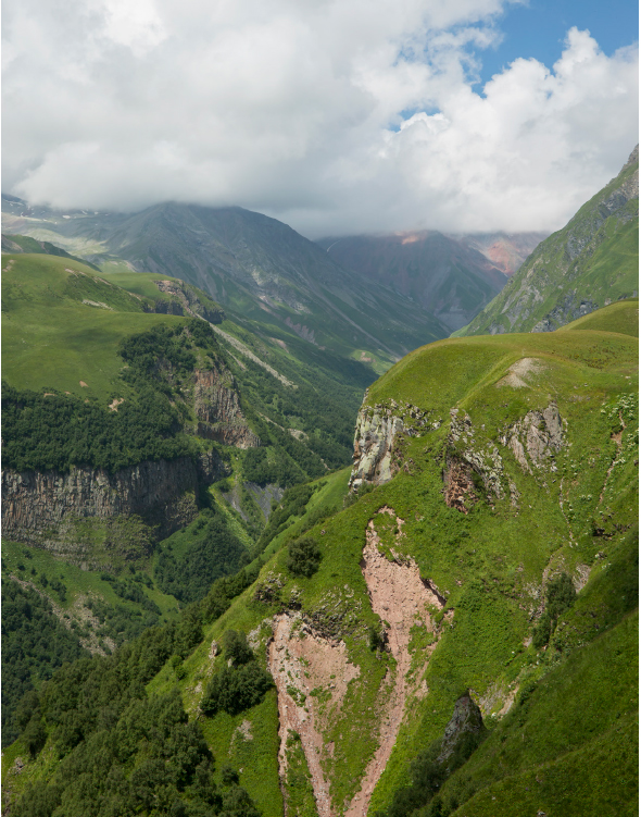 Green and rocky mountain valley with low clouds casting shadows over the landscapes