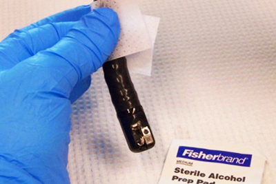 Image of blue gloved hand disinfecting a duodenoscope with an alcohol prep pad.