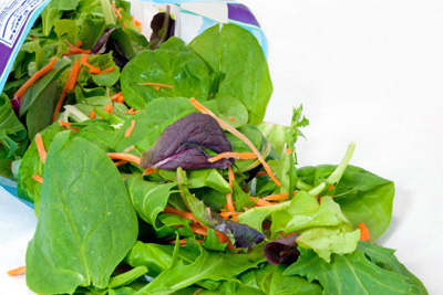 A spilled bagged salad of mixed greens on a white background