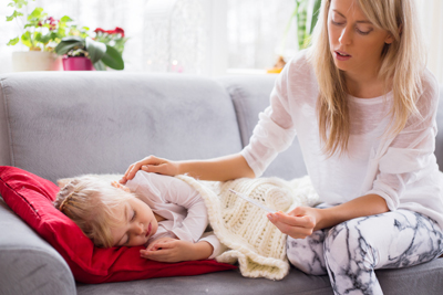 Mother looking at a thermometer in one hand, other hand resting on sick child