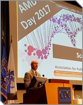 Scott Becker talking from the podium with the words screen behind him saying AMD Day 2017