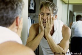 a man looking in the mirror with his hands on his face