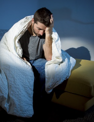 a man seated on a bed wrapped in a comforter