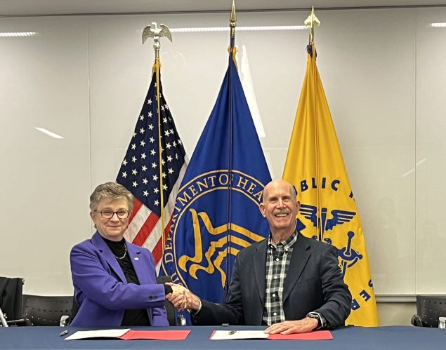 a smiling woman and man sit a table shaking hands.