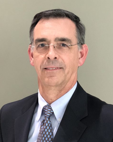 Photo of middle aged white main in black suit and tie looking at camera.