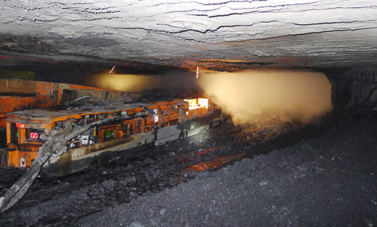 A continuous miner machine generates dust while cutting coal from the coal face.