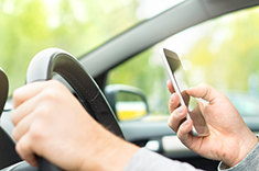 person with one hand on steering wheel the other holding cell phone