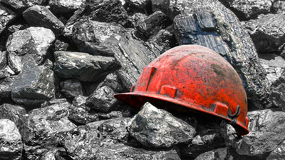 Red hard hat covered with coal dust sitting on pile of coal.