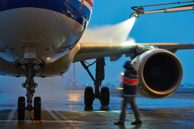 Worker de-icing plane on air strip.