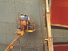 Workers using powered manlift along the side of a ship.