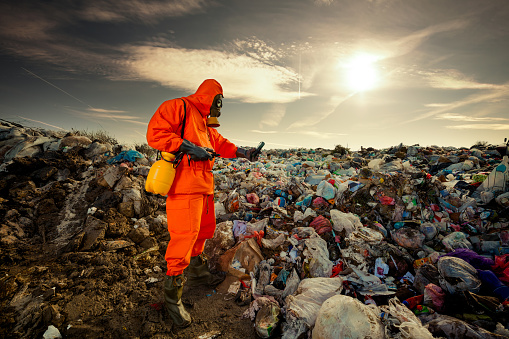 Worker in haz mat suit and full breathing mask standing in waste pit.