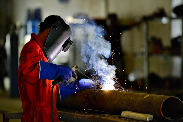 Image of worker wearing personal protective clothing welding a large pipe.