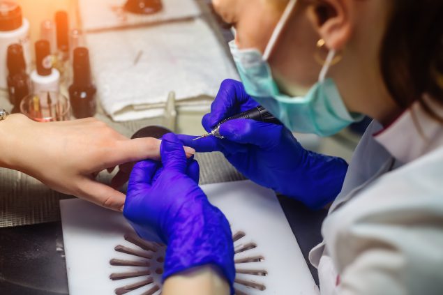 Technician working in nail salon wearing latex gloves and breathing mask.