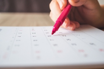 Hand with pen writing on calendar page closeup